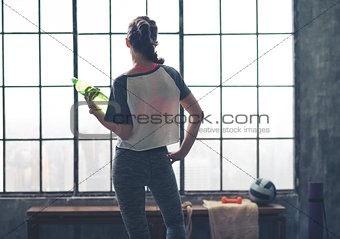 Rear view of woman looking out of loft gym holding water bottle