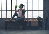 Fit woman in profile sitting on bench in loft gym drinking water