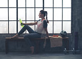 Fit woman sitting on bench in loft gym holding water bottle
