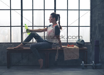 Fit woman sitting on bench in loft gym holding water bottle