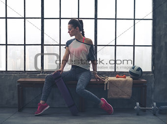 Woman in workout gear posing in profile on loft gym bench