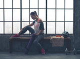 Fit woman in workout gear sitting on bench in loft gym