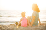Mother smiling over shoulder sitting next to daughter on beach