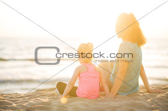 Mother smiling over shoulder sitting next to daughter on beach