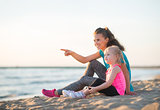 Pointing mother with daughter in workout gear sitting on beach