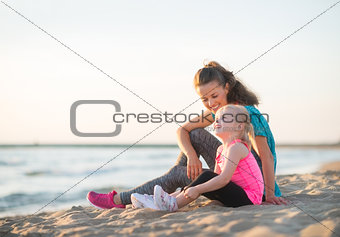 Happy young mother and daughter talking and sitting on the beach