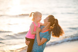 Happy mother holding daughter in her arms by water on beach