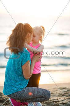 Fit young mother and daughter on beach giving Eskimo kisses
