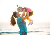 Happy mother holding child up in air at the beach at sunset