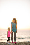 Fit young mother and daughter walking and holding hands on beach