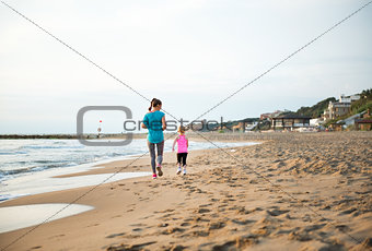 Seen from behind, mother and daughter running on the beach
