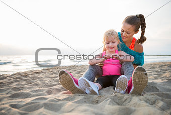 Fit young mother and daughter sitting on the beach at sunset