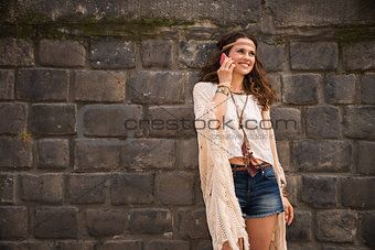 happy boho young woman near stone wall talking cell phone