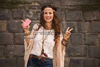 happy boho young woman near stone wall showing victory gesture