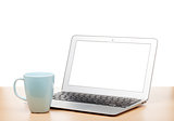 Laptop with blank screen and cup on table