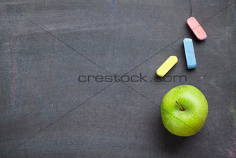 Colorful chalk and apple on blackboard background