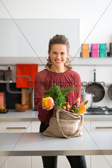 Happy woman with bag of fresh produce holding out an apple