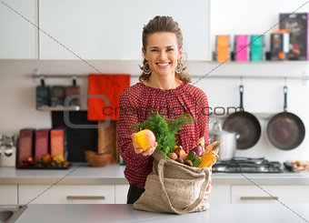 Smiling woman with bag of fresh produce holding up an apple