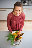 Happy woman in kitchen looking up holding bag of fall veggies