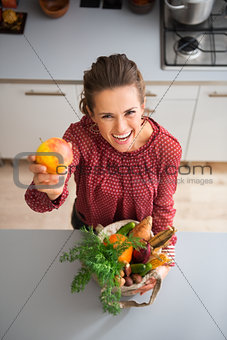 Happy woman holding up apple while holding fall vegetables