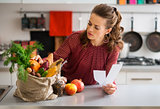 Woman in kitchen holding shopping list looking through items