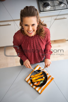 Smiling woman looking up in kitchen cutting roasted vegetables
