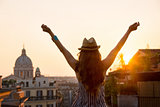 Woman from behind with outstretched arms in Rome at sunset
