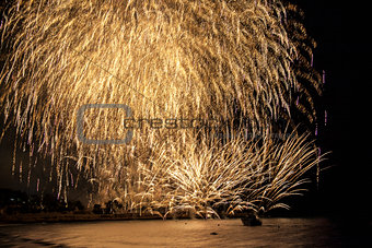 Golden fireworks falling over sea with reflections