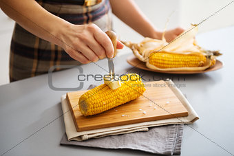 A woman's hand putting butter on corn on the cob on board