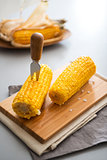 Two corn cobs on a wooden board with a corn skewer