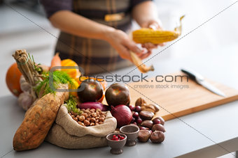 Autumn vegetables in a kitchen with anonymous woman husking corn