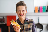 Closeup of smiling woman holding up a corn cob with its husk