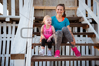 Mother and daughter in fitness gear sitting on beach hut steps