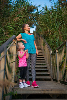 Happy woman and daughter in fitness gear on steps at beach
