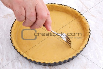 Woman using fork to prick holes in an uncooked pie crust