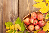 Apples in bowl and colorful autumn leaves on wooden background