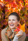 Portrait of cheerful woman with autumn leafs in front of foliage