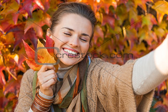 Portrait of happy relaxed woman with autumn leafs making selfie