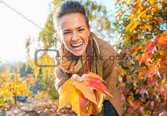 Laughing woman holding colorful autumn leafs in city park