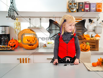 Funny girl in halloween bat costume in decorated kitchen