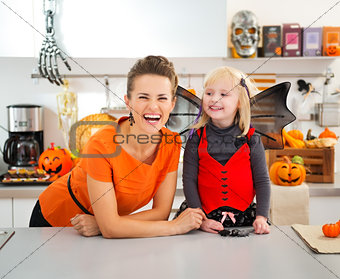 Funny girl in halloween bat costume with mother in kitchen