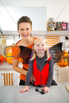 Happy girl in halloween bat costume with mother in kitchen