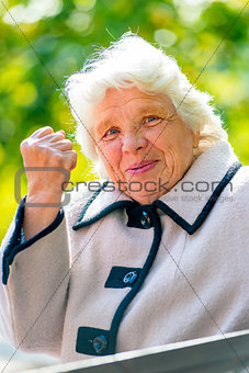 gray-haired old lady shows a fist in the park