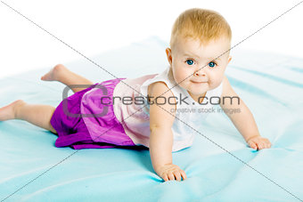 baby girl in a dress creeps on the blue coverlet