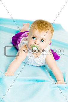 baby girl with pacifier crawling on the blue coverlet