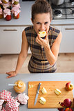 Happy woman biting into apple quarter in kitchen