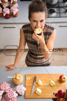 Happy woman biting into apple quarter in kitchen