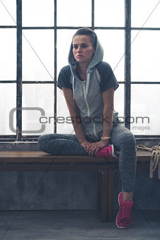 Fit woman sitting on loft gym bench leaning against bent leg