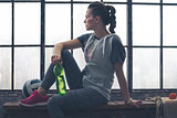 Woman in workout gear sitting on bench in city loft looking out