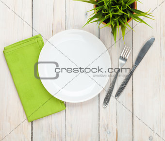 Empty plate and silverware over white wooden table background